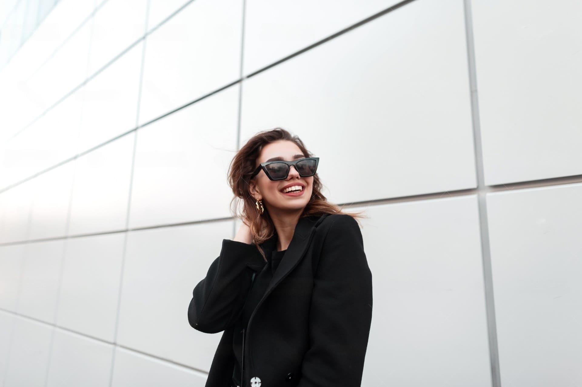 young woman in a long black jacket wearing sunglasses and smiling